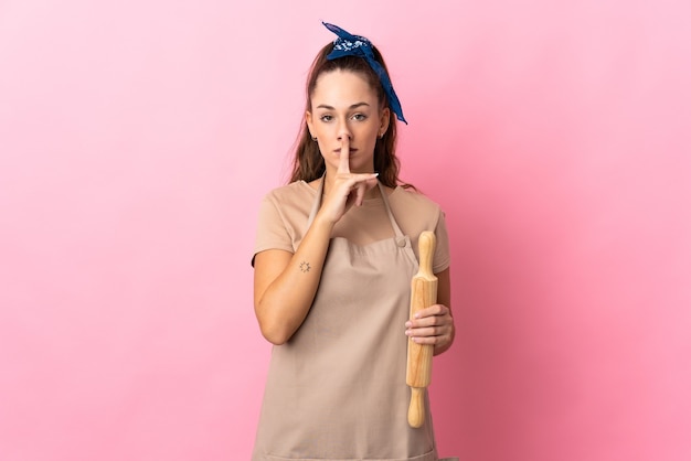Young woman holding a rolling pin showing a sign of silence gesture putting finger in mouth