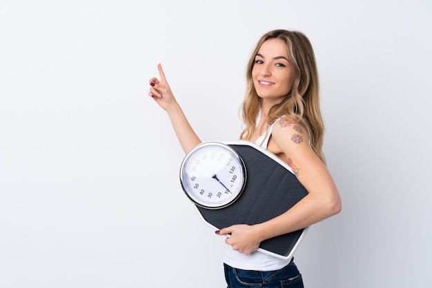 Young woman holding a scale over  wall