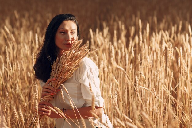 Young Woman holding sheaf of wheat ears at agricultural field.