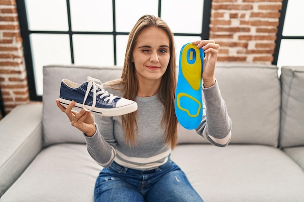 Young woman holding shoe insole winking looking at the camera with sexy expression, cheerful and happy face.