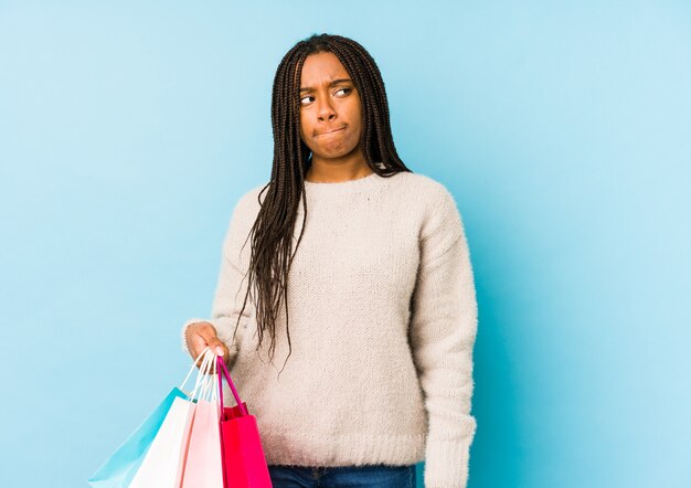 Young woman holding a shopping bag confused, feels doubtful and unsure