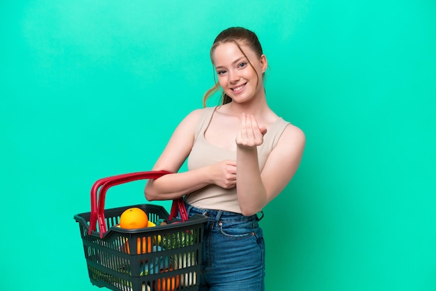 Young woman holding a shopping basket full of food isolated on green background