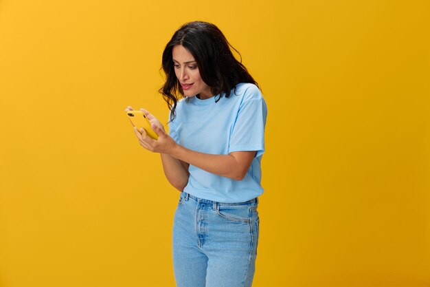 Young woman holding smart phone against yellow background