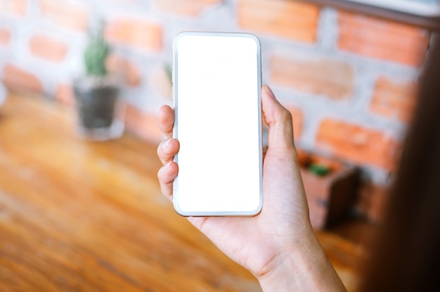 Foto smart phone della tenuta della giovane donna con lo schermo in bianco mentre sedendosi al salone.