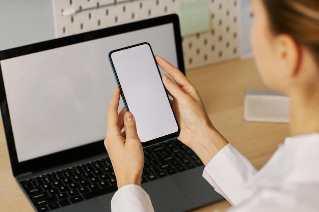 Young woman holding smartphone with white screen mockup at desk