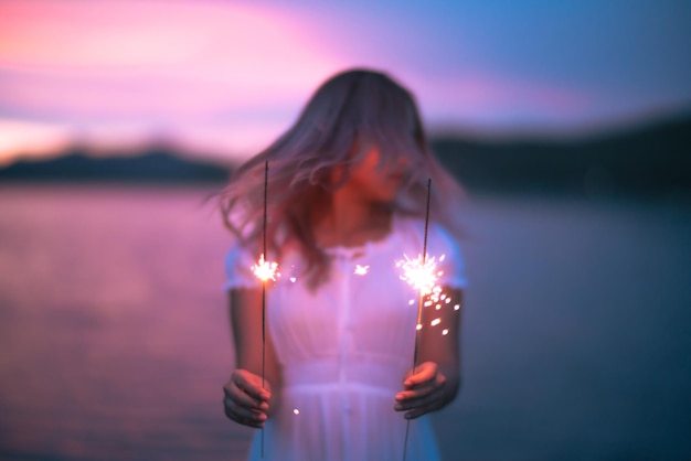 Photo young woman holding sparkler standing against lake