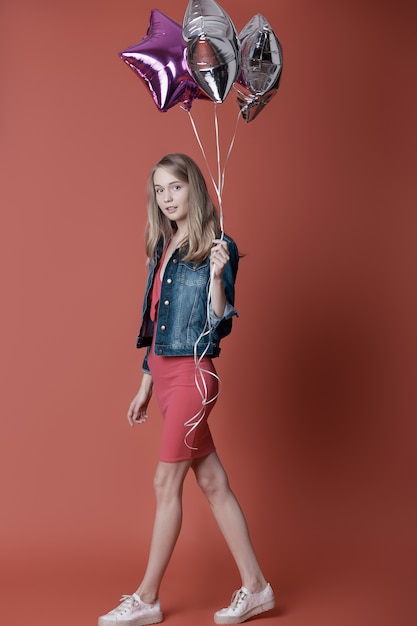 Young woman holding star balloons on red wall