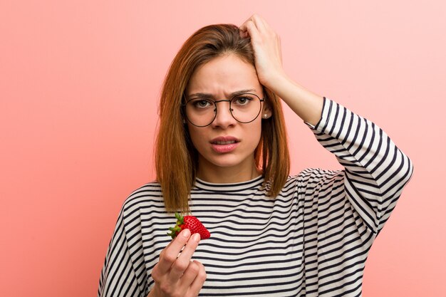 Young woman holding a strawberry being shocked, she has remembered important meeting.