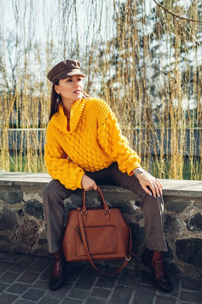 세련 된 핸드백을 들고 야외에서 노란색 스웨터를 입고 젊은 여자. 봄 여성 의류 및 액세서리. 패션. 2021 년의 색