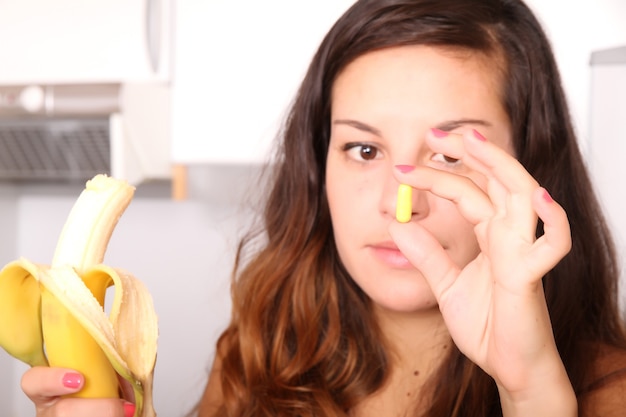 Foto una giovane donna che tiene una pillola di supplemento in una mano e una banana nell'altra.