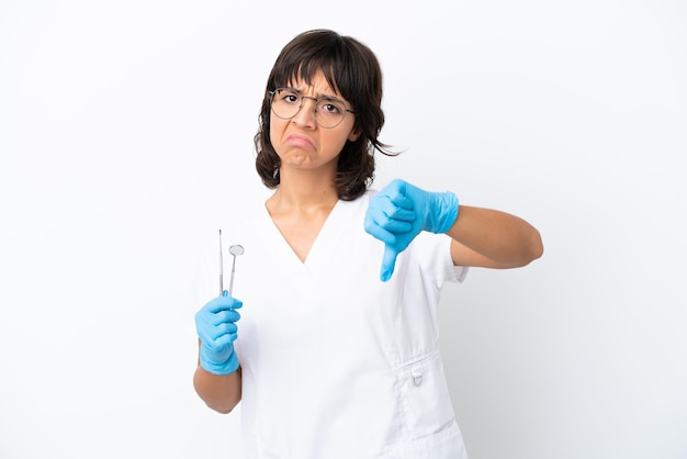 Young woman holding tools isolated on white background showing thumb down with negative expression