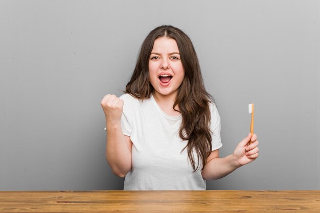 Young woman holding a toothbrush cheering carefree and excited.