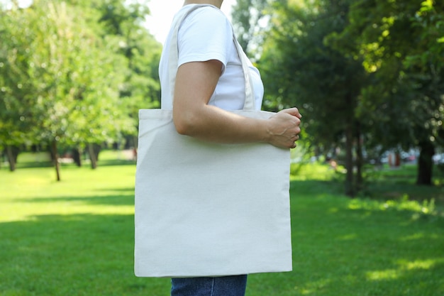 Young woman holding tote bag against greenery background