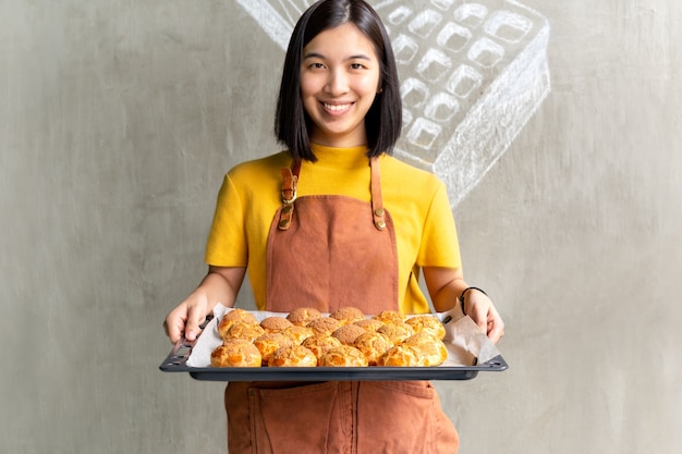 新鮮なChouxクリームまたはeclairとトレイを保持している若い女性。