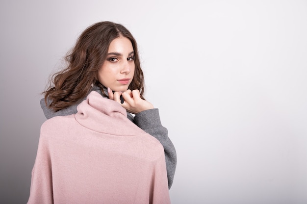 Young woman holding a turtleneck on a hanger, close up portrait with copy space. Shopping and consumerism or stylist concept. Seasonal updates in clothing store . 