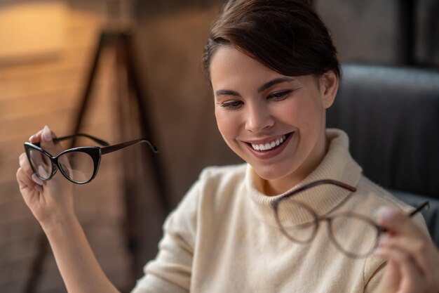 A young woman holding two pairs of eyeglasses and smiling