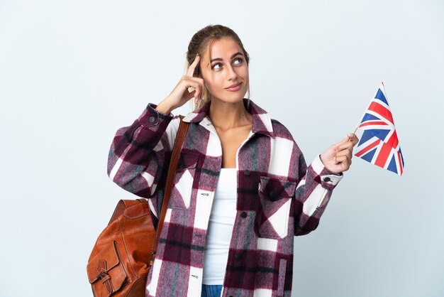 Young woman holding an UK flag isolated on white space having doubts and thinking