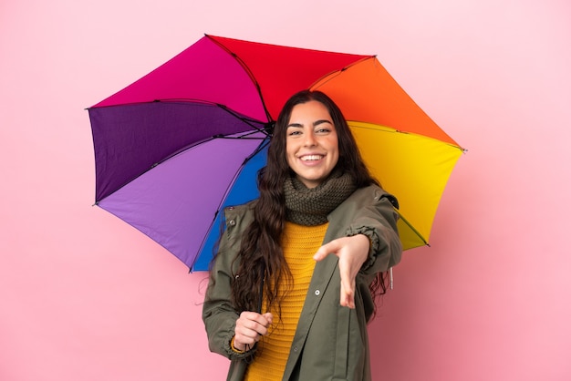 Молодая женщина, держащая зонтик на розовом фоне, пожимая руку для заключения хорошей сделки