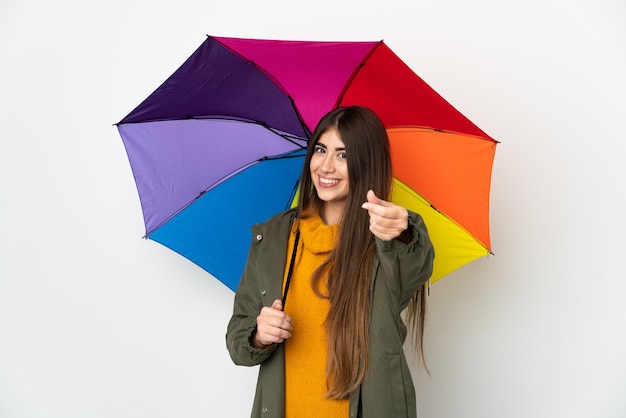 Young woman holding an umbrella isolated on white background making money gesture