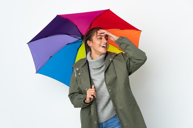 Young woman holding an umbrella isolated on white wall smiling a lot