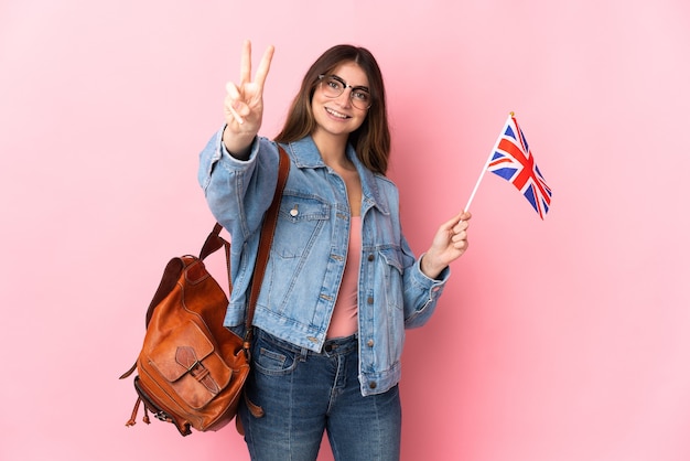 Young woman holding an United Kingdom flag isolated on pink wall smiling and showing victory sign