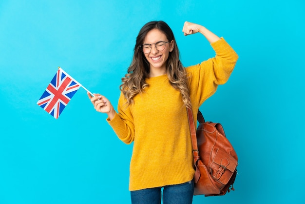 Young woman holding an United Kingdom flag posing isolated against the blank wall