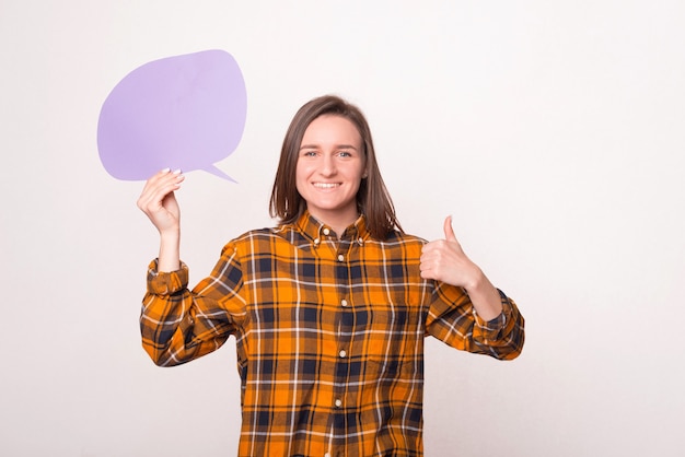 Молодая женщина держит фиолетовый пустой речевой пузырь и показывает палец вверх