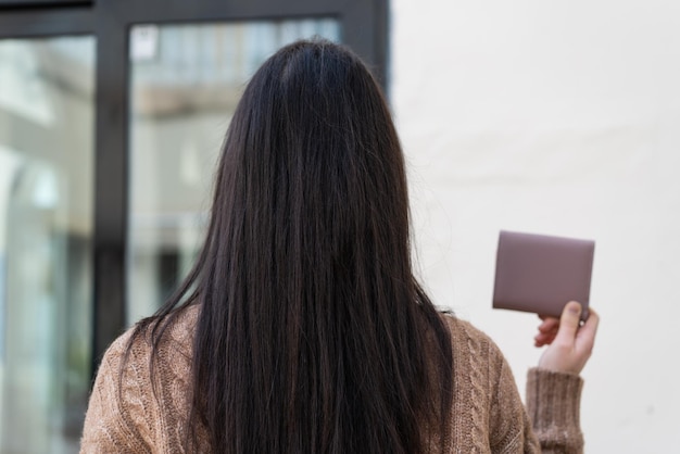 バックの位置で屋外で財布を保持している若い女性