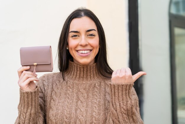 屋外で財布を持って横を指差して製品を提示する若い女性