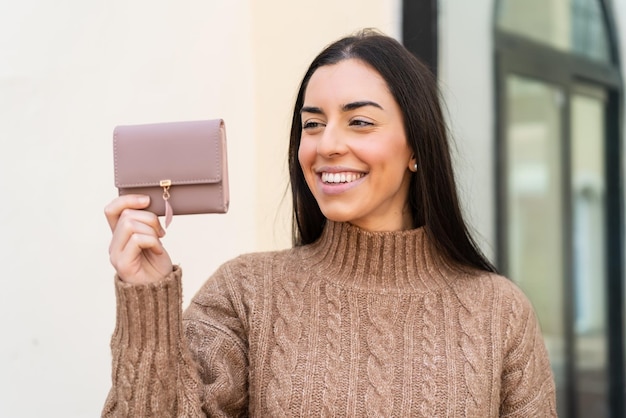 Young woman holding a wallet at outdoors with happy expression