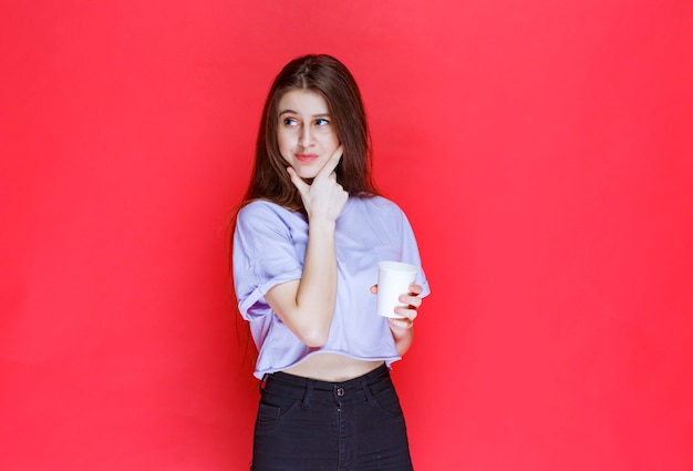 young woman holding a white disposable water cup and thinking.