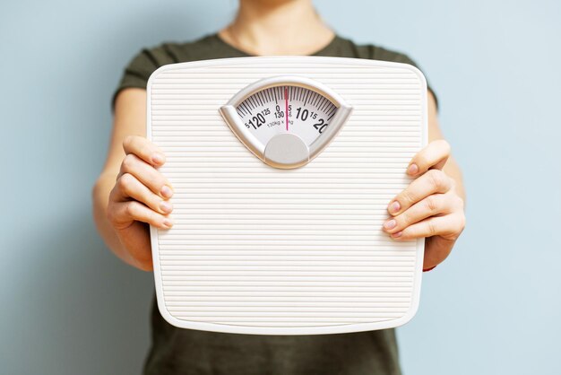 Photo young woman holding white scales to check the results of her diet