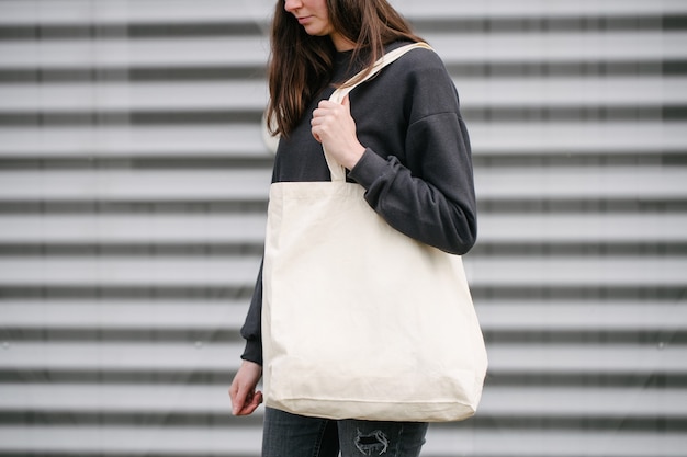 Young woman holding white textile eco bag against urban city