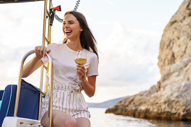 Young woman holding a wineglass and sitting on deck of sailing yacht