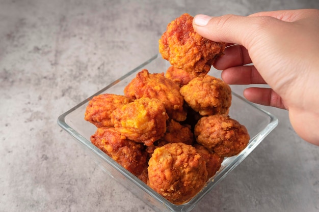 Young woman holding with her hand piece of fried chicken ready to eat as an appetizer in glass bowl