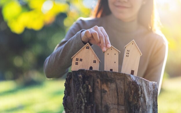 A young woman holding wooden house models on tree stump in the outdoors