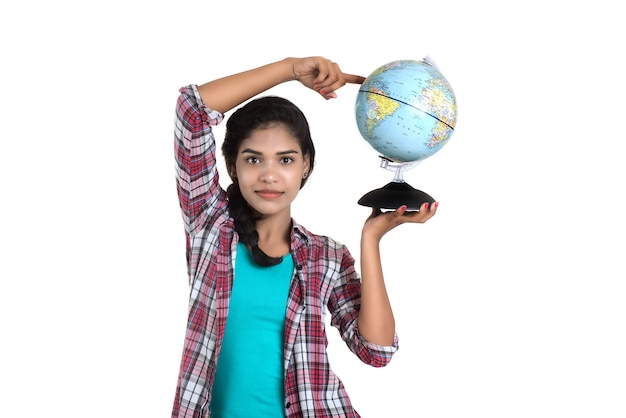 Young woman holding the world globe and posing on a white wall.