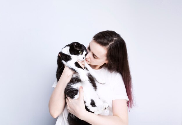 Young woman holds adult cat, grey background