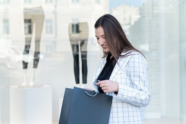 Young woman holds black package for purchases against showcase backdrop. Sale.