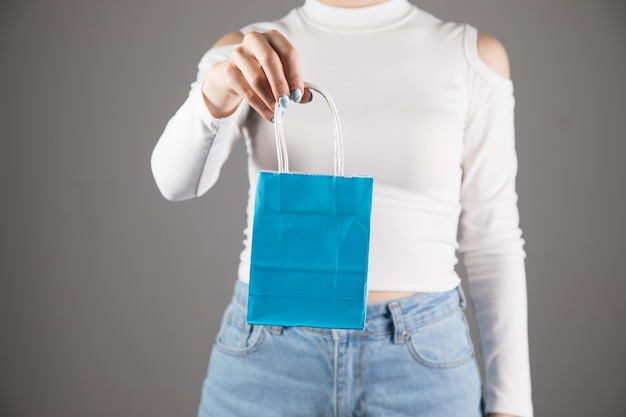 Young woman holds a blue gift bag on a gray wall