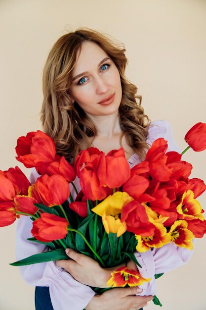 A young woman holds a bouquet of red tulips The concept of March 8 Valentine's Day A beautiful gift for a girl Spring portrait of a woman
