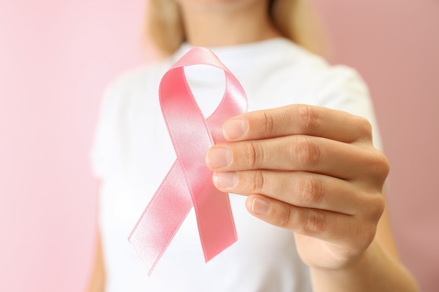 Young woman holds breast cancer awareness ribbon, close up