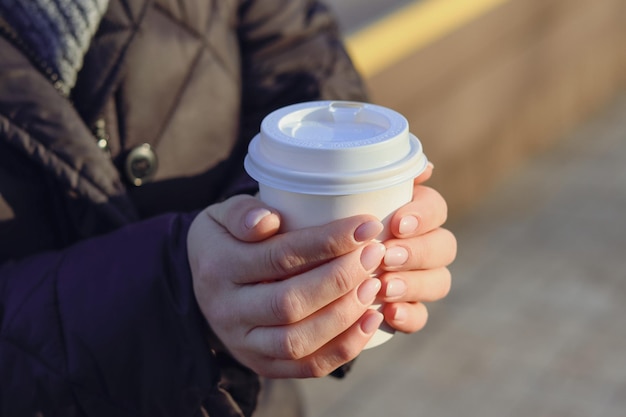 A young woman holds a disposable cup of coffee outside in the park