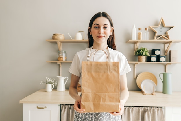 Young woman holds eco shopping paper bag with food in hands in  kitchen