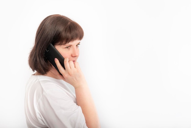 Young woman holds her phone near her ear. Portrait of dark-haired girl with mobile phone on white background.