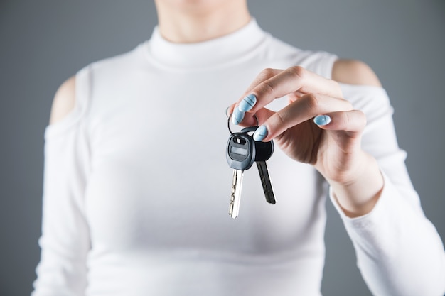 Young woman holds the keys to the house on a gray wall