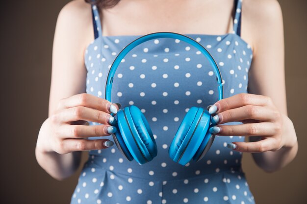 Young woman holds large headphones on a brown background