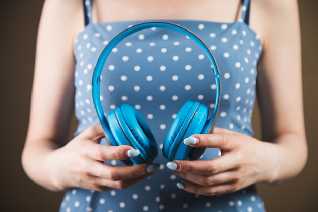 Young woman holds large headphones on a brown background