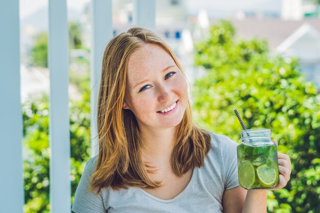 Young woman holds a mason jar in her hand with a mojito