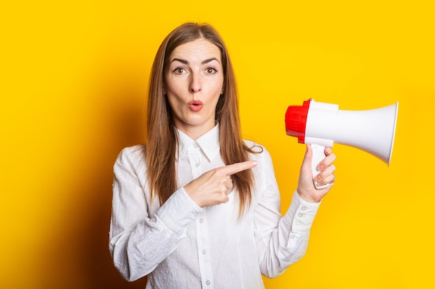 Young woman holds a megaphone in her hands and points her finger at it on a yellow background Hiring concept help wanted Banner